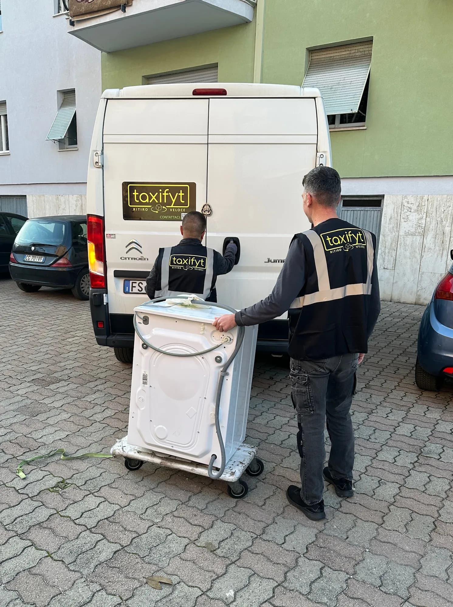 Due trasportatori TaxiFyt portano una lavatrice su un carrello verso il furgone